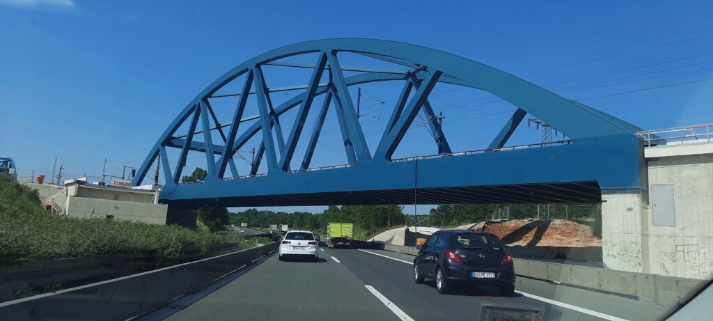 Blauer Stahlbogenbrücke, die über eine Autobahn mit Fahrzeugen führt.
