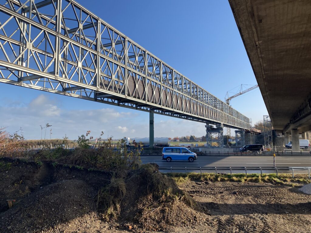 Bau einer Brücke mit Stahlträgern über einer Straße, die von Fahrzeugen befahren wird.