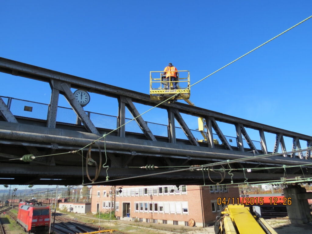 Arbeiter auf einer Hebebühne, die eine Brücke inspizieren, mit einem klaren blauen Himmel im Hintergrund.
