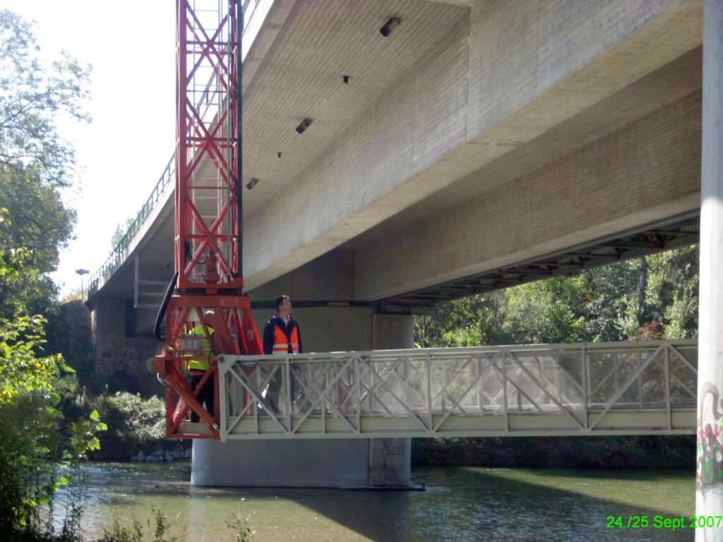 Bauarbeiter auf einer Brücke mit einem Kran und einer Stahlkonstruktion über einem Gewässer.