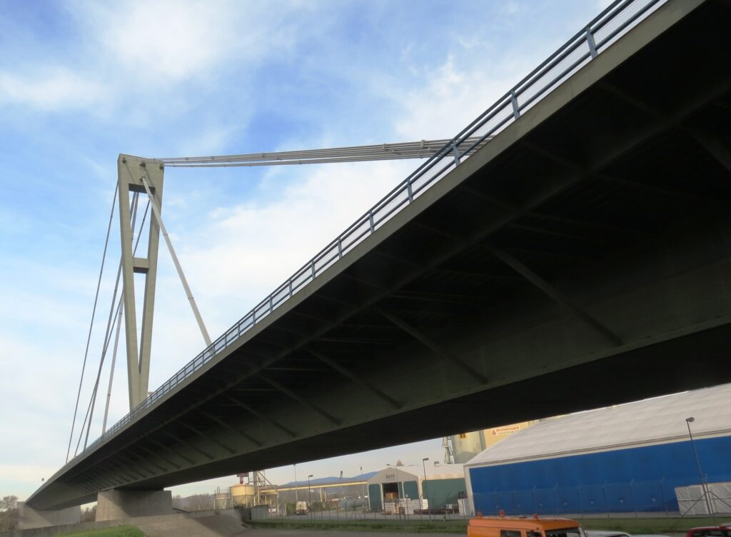 Moderne Brücke mit einer schrägen Seilstruktur und Betonpfeilern, die über einen Wasserweg führt.