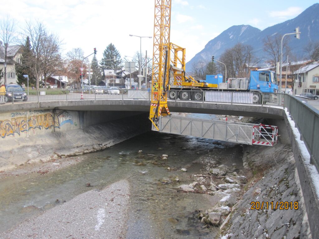 Baukran über einer Brücke, die über einen Fluss führt, mit einem Lkw im Hintergrund.
