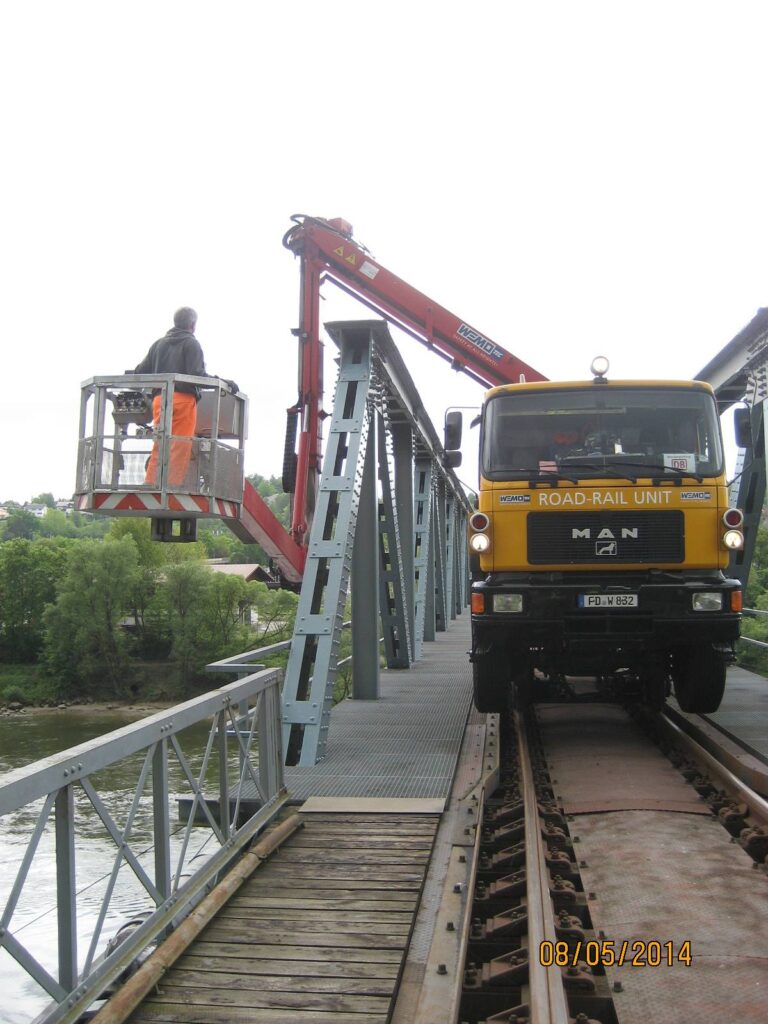 Ein MAN Lkw mit einem Kran auf einer Brücke, während eine Person in einer Hebebühne sitzt.