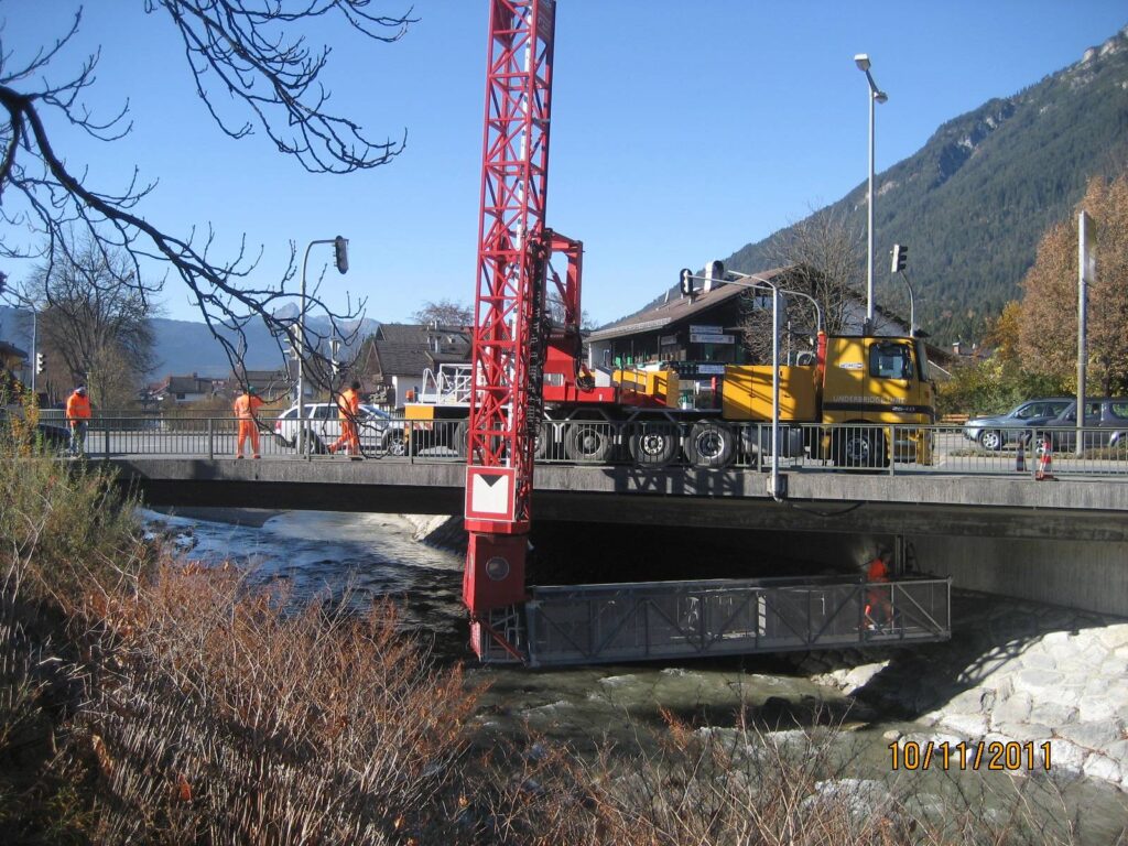 Bauarbeiten an einer Brücke mit einem Kran und einem gelben Fahrzeug auf der Fahrbahn.