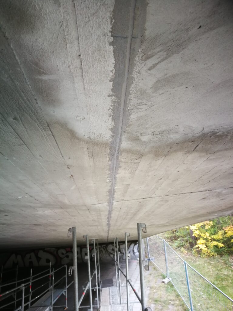 Betonunterseite mit sichtbaren Rissen und Gerüst zur Unterstützung während der Renovierung.