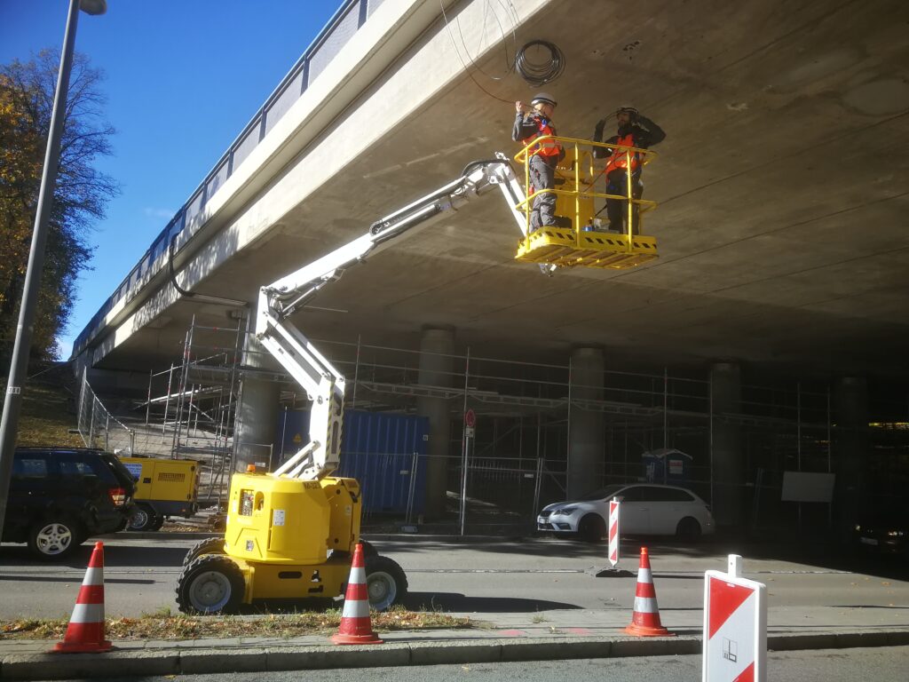 Arbeiter in einem Arbeitskorb, der an einer Brücke unterhalb einer Straße arbeitet.