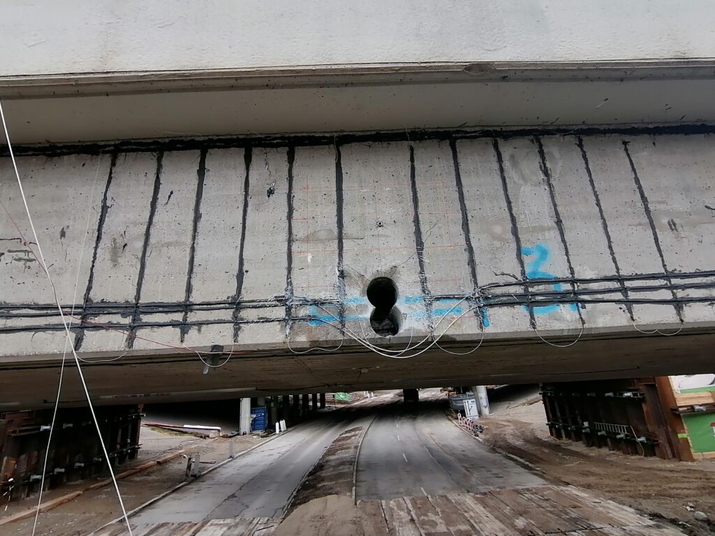 Betonträger mit sichtbarem Loch und Kabeln, die an der Unterseite befestigt sind.