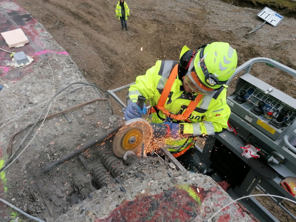 Arbeiter mit Schutzkleidung schneidet Beton mit einer Trennscheibe, Funken fliegen.